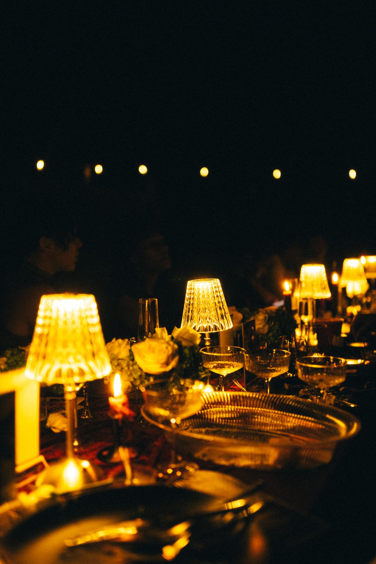 Glowing gold lamps and floral details along a velvet-draped dinner table