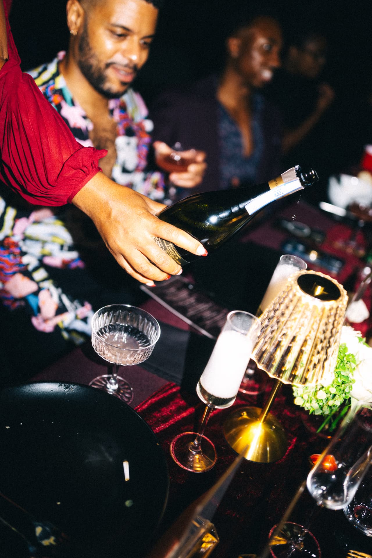 A glass of sparkling wine being poured beside a warm table lamp